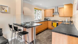 A modern kitchen with a central island, bar stools, wooden cabinets, and a gas stove. - Cosy 2 Bedr house in a central Norwich with all amenities  (Norwich)