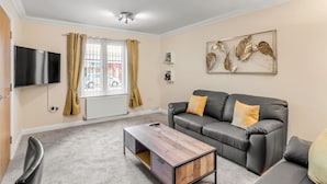 A living room with a black leather sofa, a wooden coffee table, a flat-screen TV mounted on the wall, a window with curtains, and a ceiling light fixture. - Cosy 2 Bedr house in a central Norwich with all amenities  (Norwich)