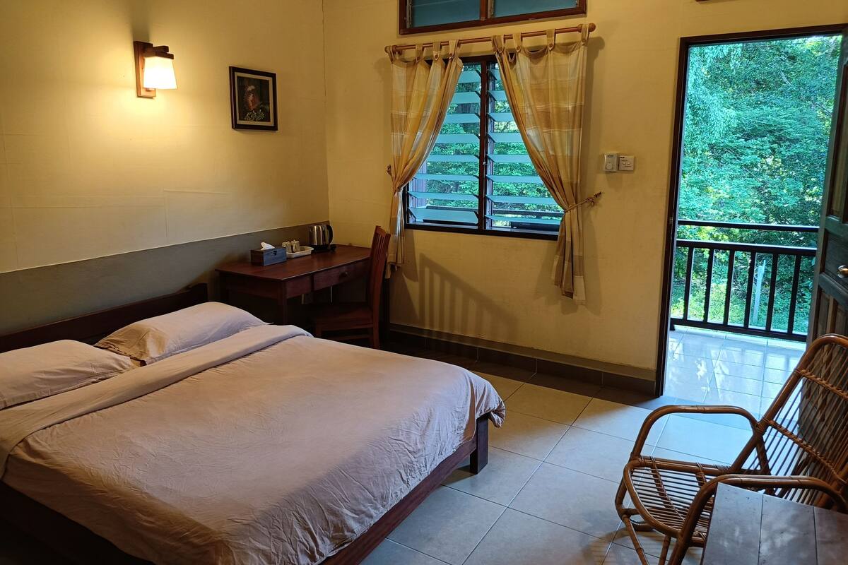 Una habitación de hotel con cama, escritorio con hervidor, silla y ventana con cortinas.