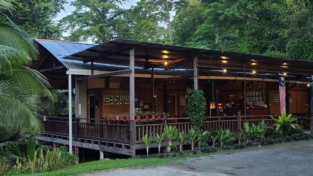 Ein hölzernes Gebäude mit überdachter Veranda, umgeben von üppigem Grün.