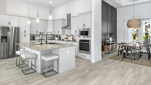 Una cocina moderna con armarios blancos, electrodomésticos de acero inoxidable y una isla central con taburetes de bar.