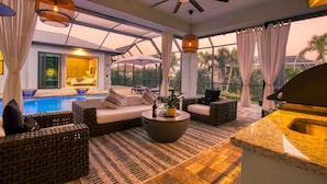 Un área de piscina interior moderna con mobiliario de mimbre, un ventilador de techo y vistas a la piscina.