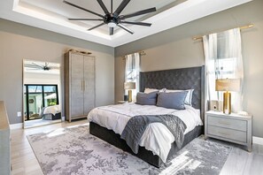 Un dormitorio moderno con una cama grande, un ventilador de techo, una mesita de noche y vistas a través de un ventanal.