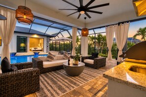A modern outdoor lounge area with a pool, wicker furniture, and a ceiling fan. - Intervillas Florida - Villa Oasis (Cape Coral)