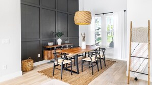 Un comedor con mesa y sillas de madera, una lámpara colgante tejida y vistas al exterior con vegetación.
