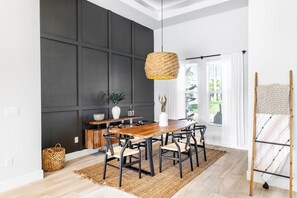 Un coin repas avec une table et des chaises en bois, un luminaire suspendu en fibres tressées et une vue sur la verdure à l’extérieur.