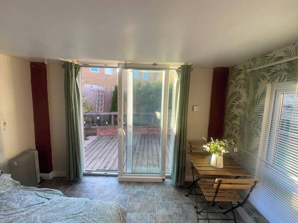 A room with a sliding glass door leading to a patio, a bed, a wooden table with a vase of flowers, and a radiator.