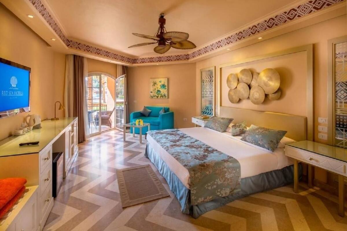 A hotel room with a bed, a desk, a television, a ceiling fan, and a window.