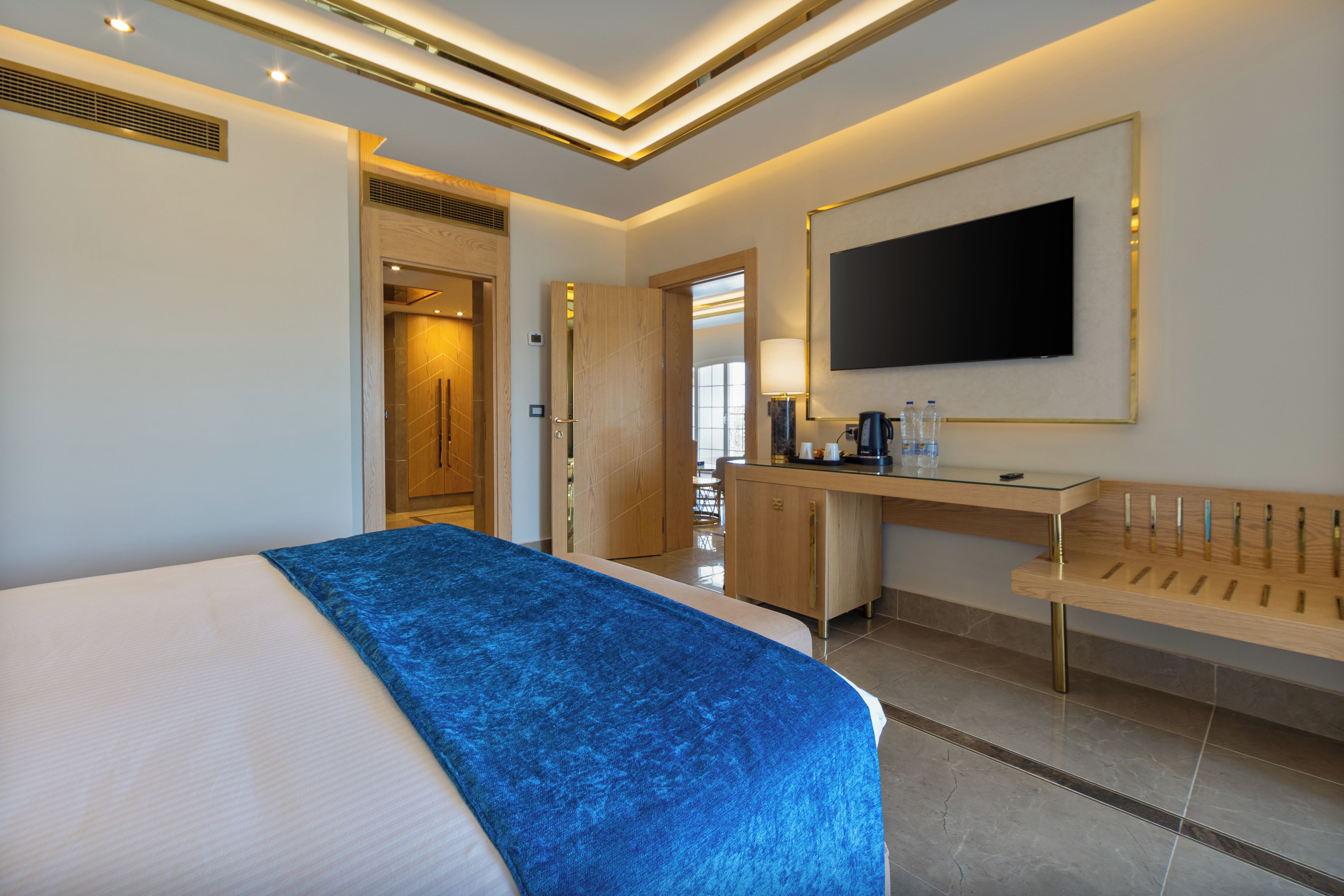 Habitación de hotel con cama, escritorio, televisor y baño visible a través de una puerta abierta.