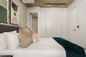 A modern bedroom with a large bed, a headboard, and a wardrobe. - The Signature 116 (Cape Town)