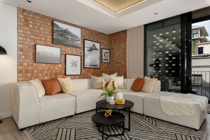 A modern living room with a brick wall, a sectional sofa, and a coffee table. - The Signature 116 (Cape Town)