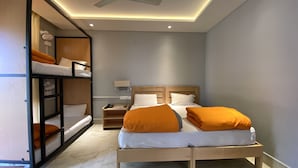 A compact hotel room with a bunk bed, a single bed, a bedside table with a lamp, and a ceiling fan. - Madpackers Bir  (Baijnath)