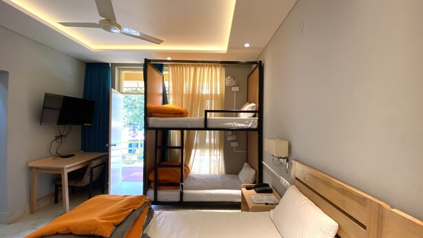 A hotel room with bunk beds, a desk with a TV, a bedside table with a lamp, and a window with curtains. - Madpackers Bir  (Baijnath)