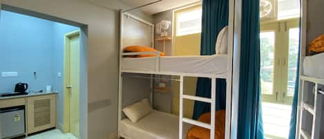 Une chambre de dortoir avec des lits superposés, un bureau avec une bouilloire et une fenêtre avec des rideaux.