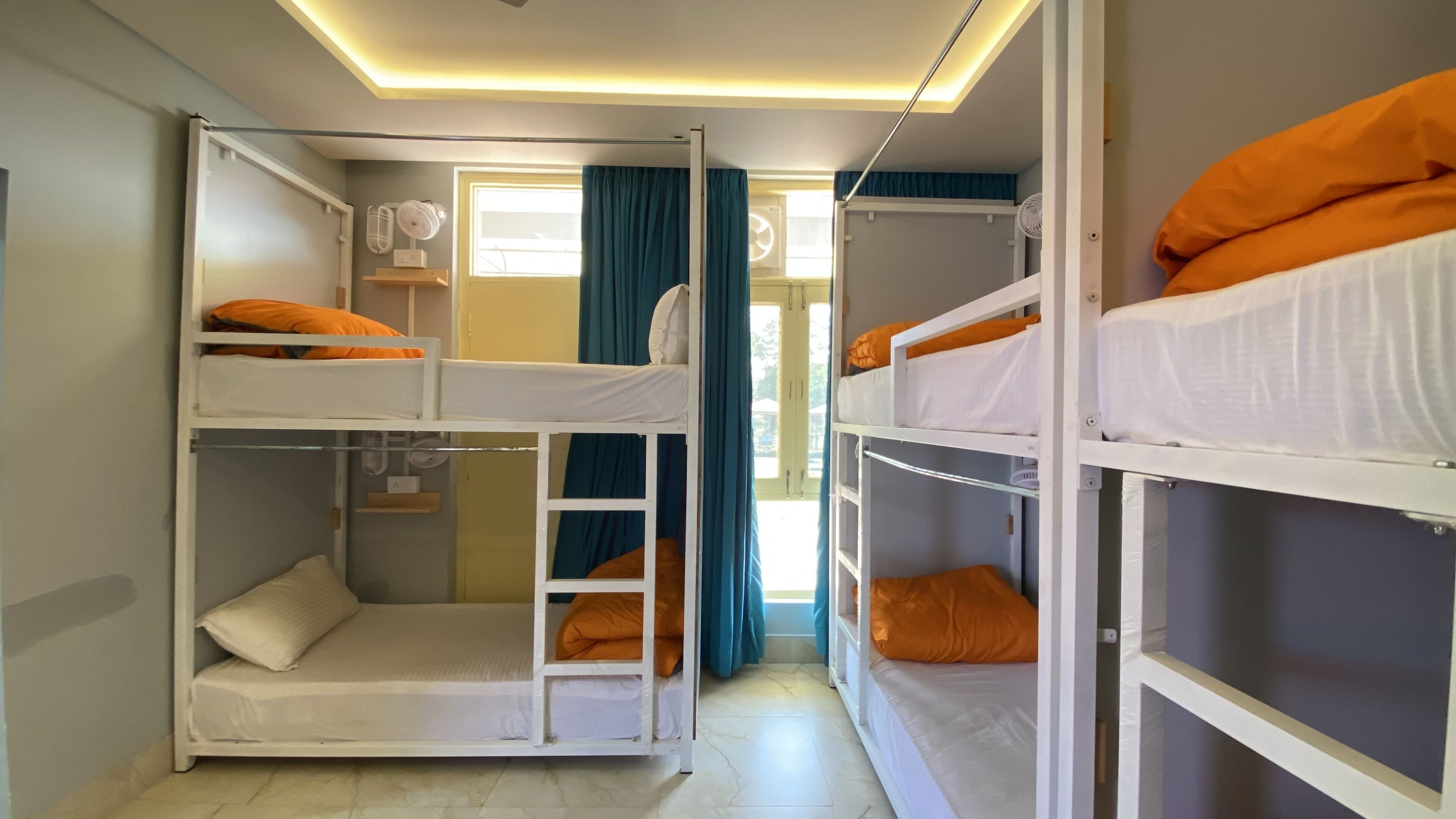 A dormitory room with bunk beds, a window with curtains, and a ceiling fan.