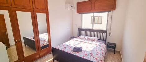 A bedroom with a bed, a wardrobe, a mirror, and a window.