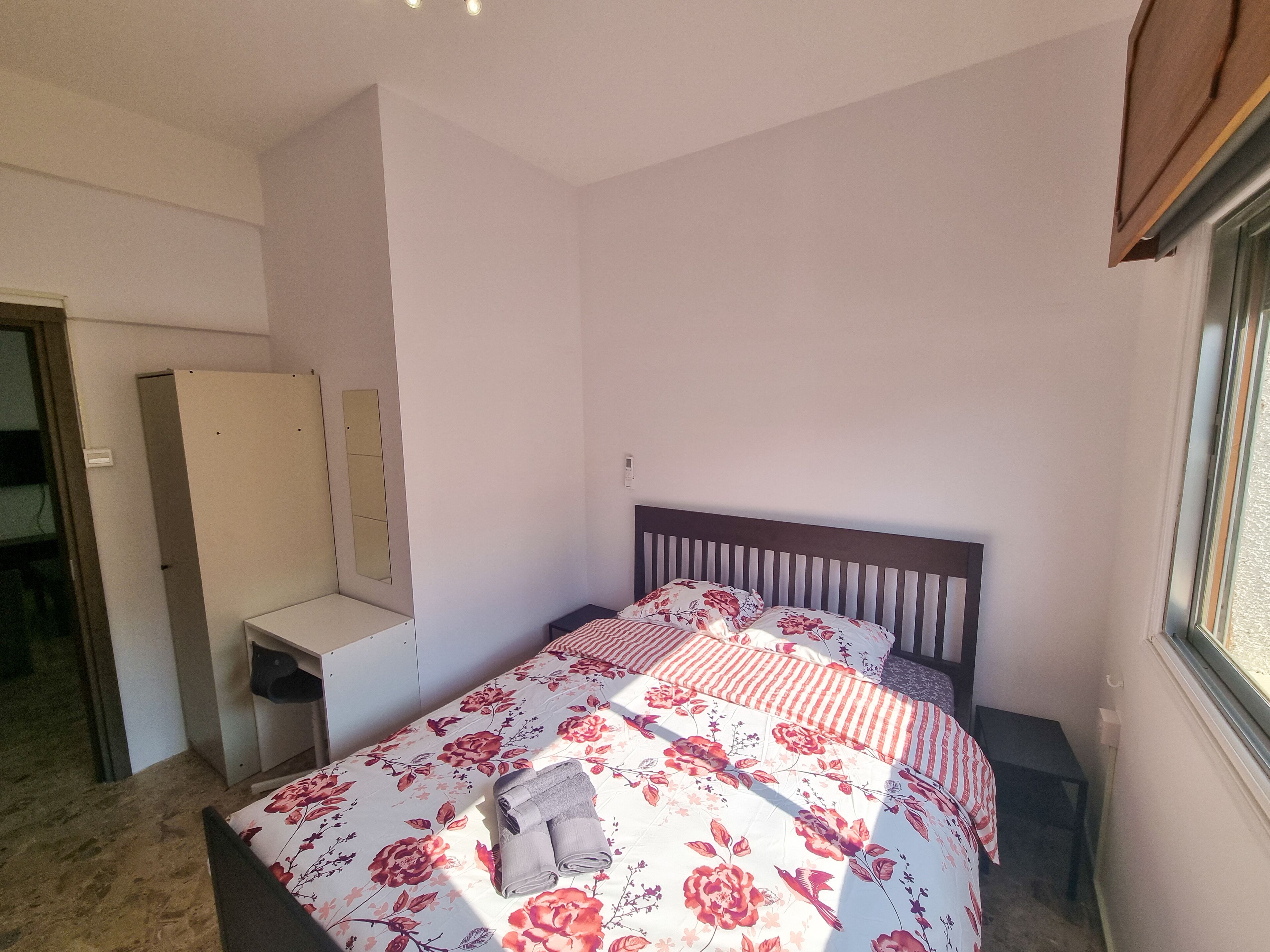A bedroom with a bed, a bedside table, a mirror, and a window.