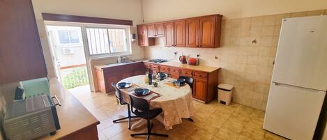 A kitchen with wooden cabinets, a dining table set for two, a refrigerator, and a ceiling fan.