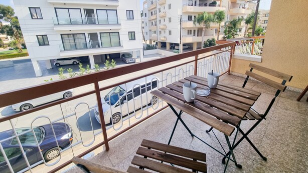 Ein Balkon mit Holzbanken und einem Tisch, mit Blick auf eine Straße mit Autos und Gebäuden.