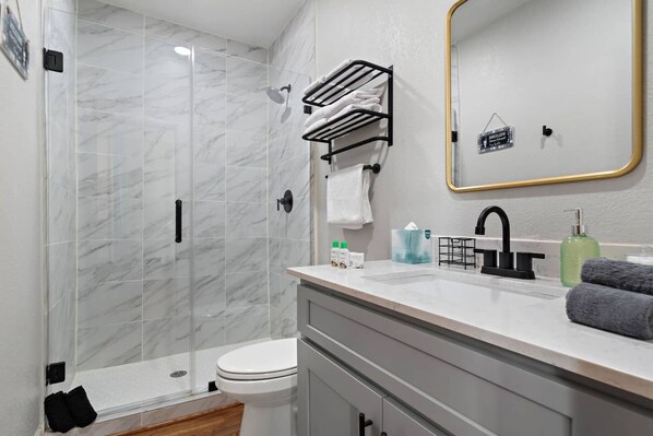 A modern bathroom with a glass-enclosed shower, a white toilet, a vanity with a sink, and a mirror with a gold frame.