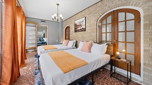 A hotel room with two beds, a brick wall, a wooden door, and a chandelier.