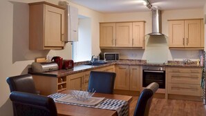 Una cucina compatta con mobili in legno, un forno a microonde, un bollitore e un'area pranzo con tavolo e sedie.