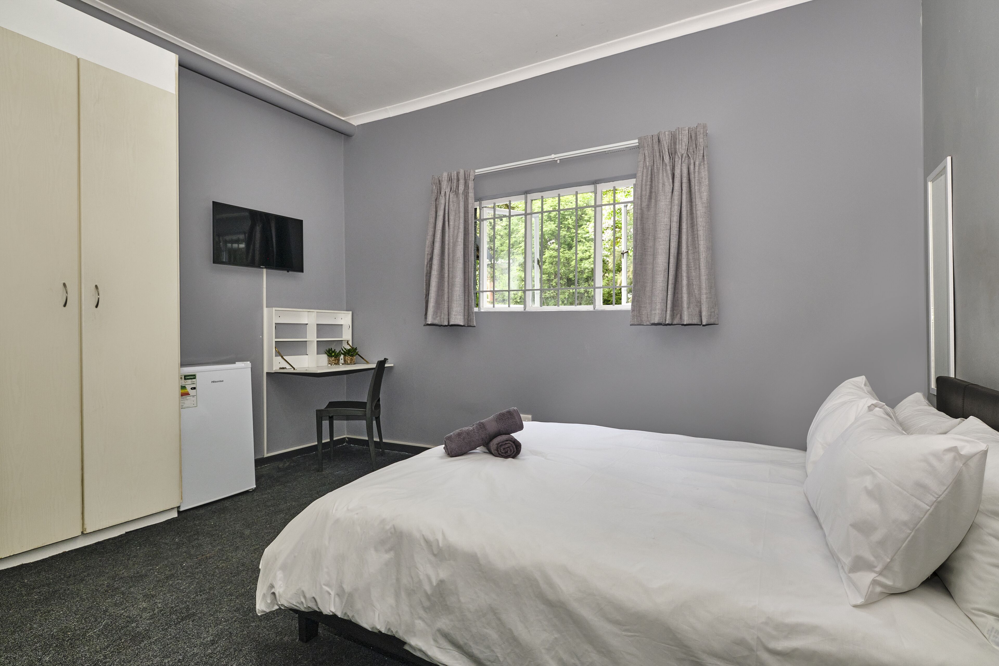 Ein Hotelzimmer mit Bett, Schreibtisch, Sessel, Fernseher und Kleiderschrank.