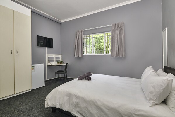 A hotel room with a bed, a desk, a chair, a TV, and a wardrobe. - Inn & Out Sandton (Sandton)