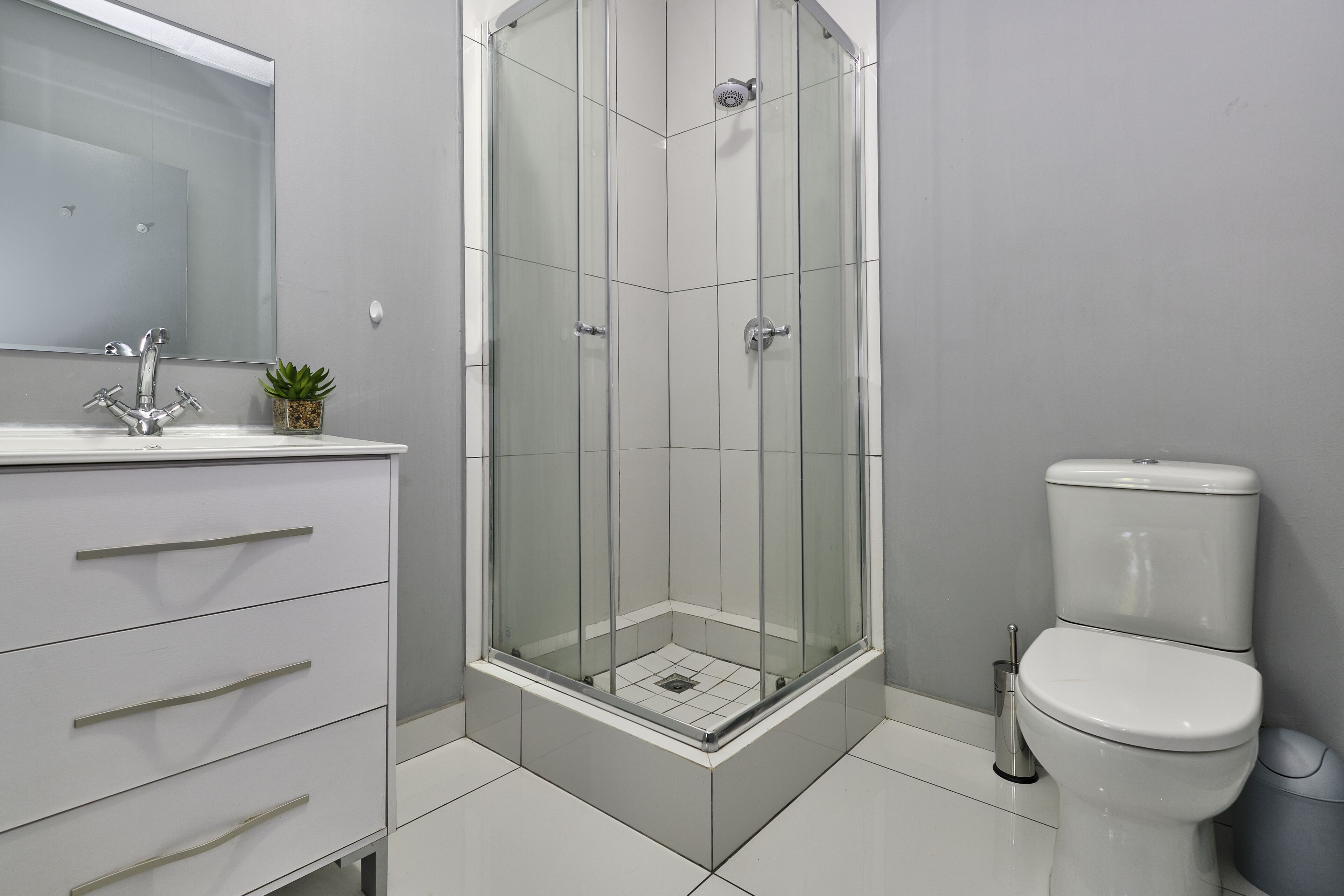 A modern bathroom with a glass-enclosed shower, a white toilet, and a vanity with drawers.