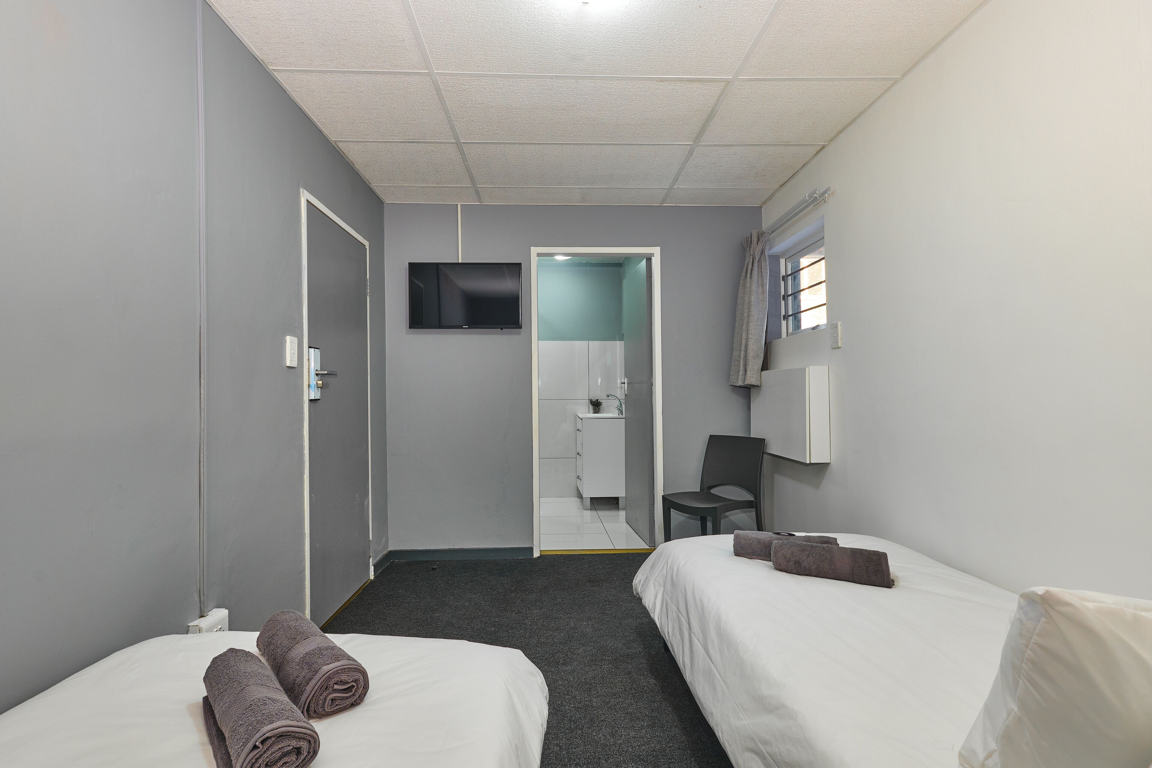 A hotel room with two beds, a TV, a desk, and a bathroom visible through an open door.