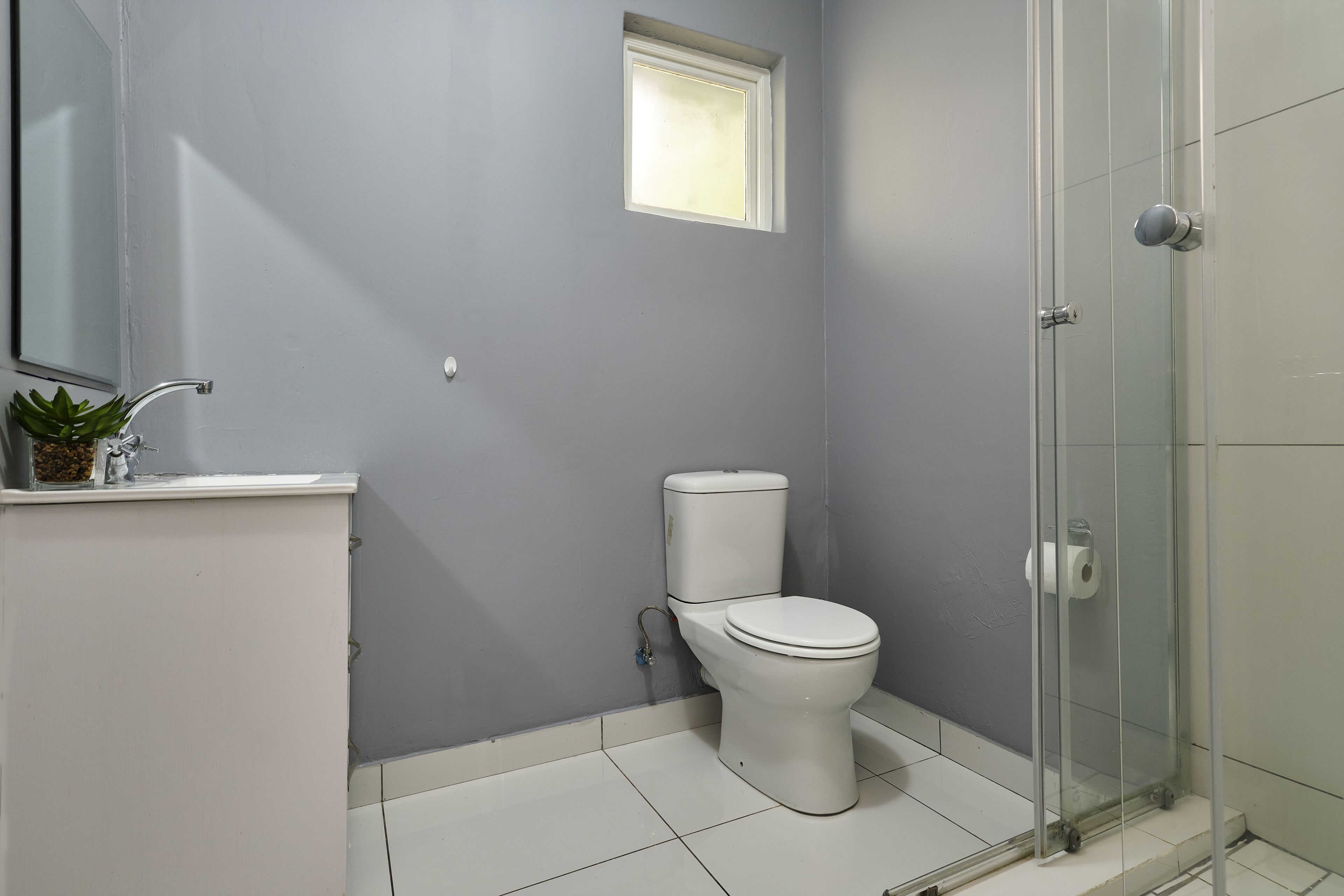 Un baño con inodoro, lavamanos, un ventanal pequeño y una cabina de ducha de vidrio.