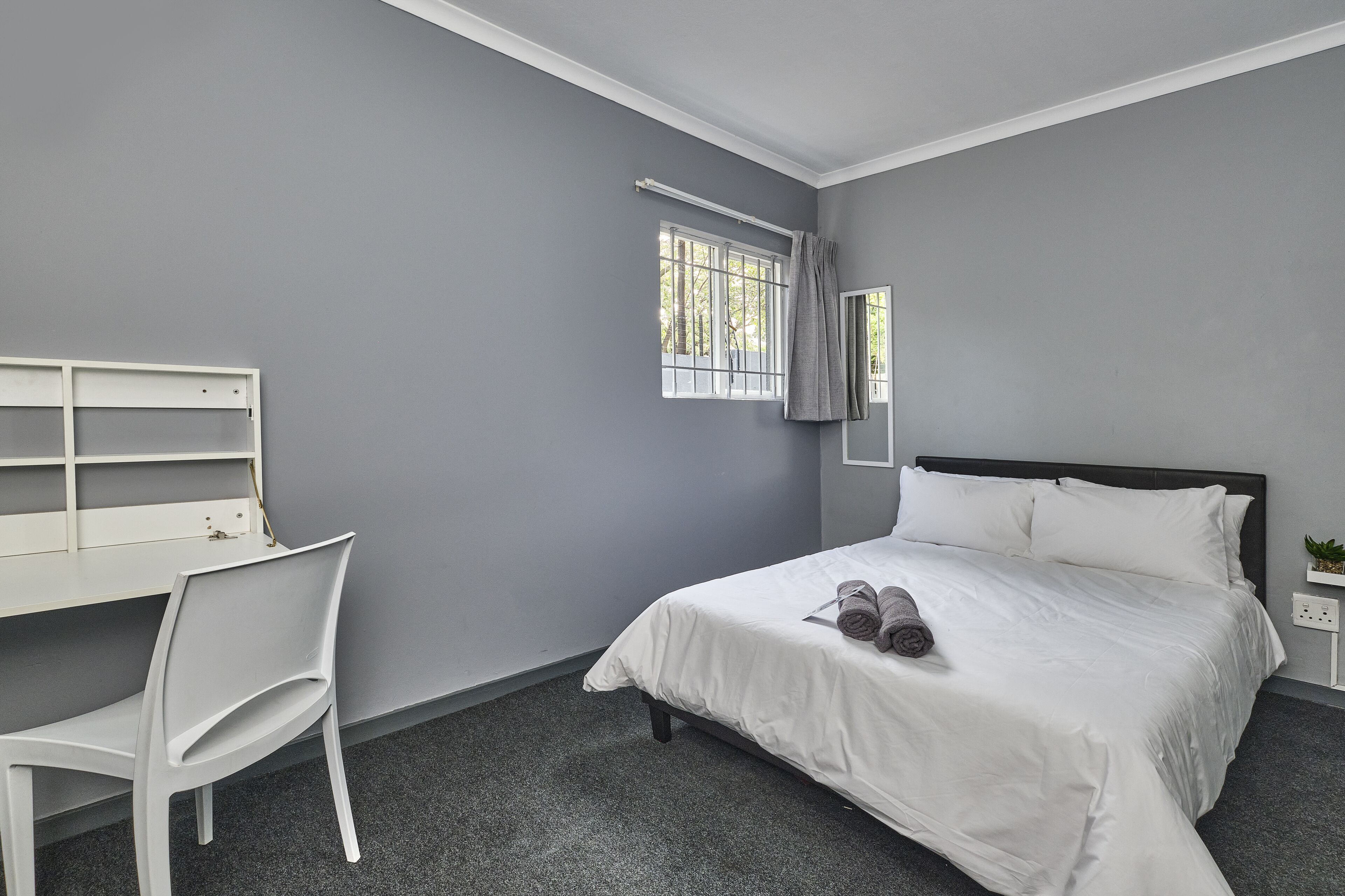 A bedroom with a bed, a desk, and a chair.
