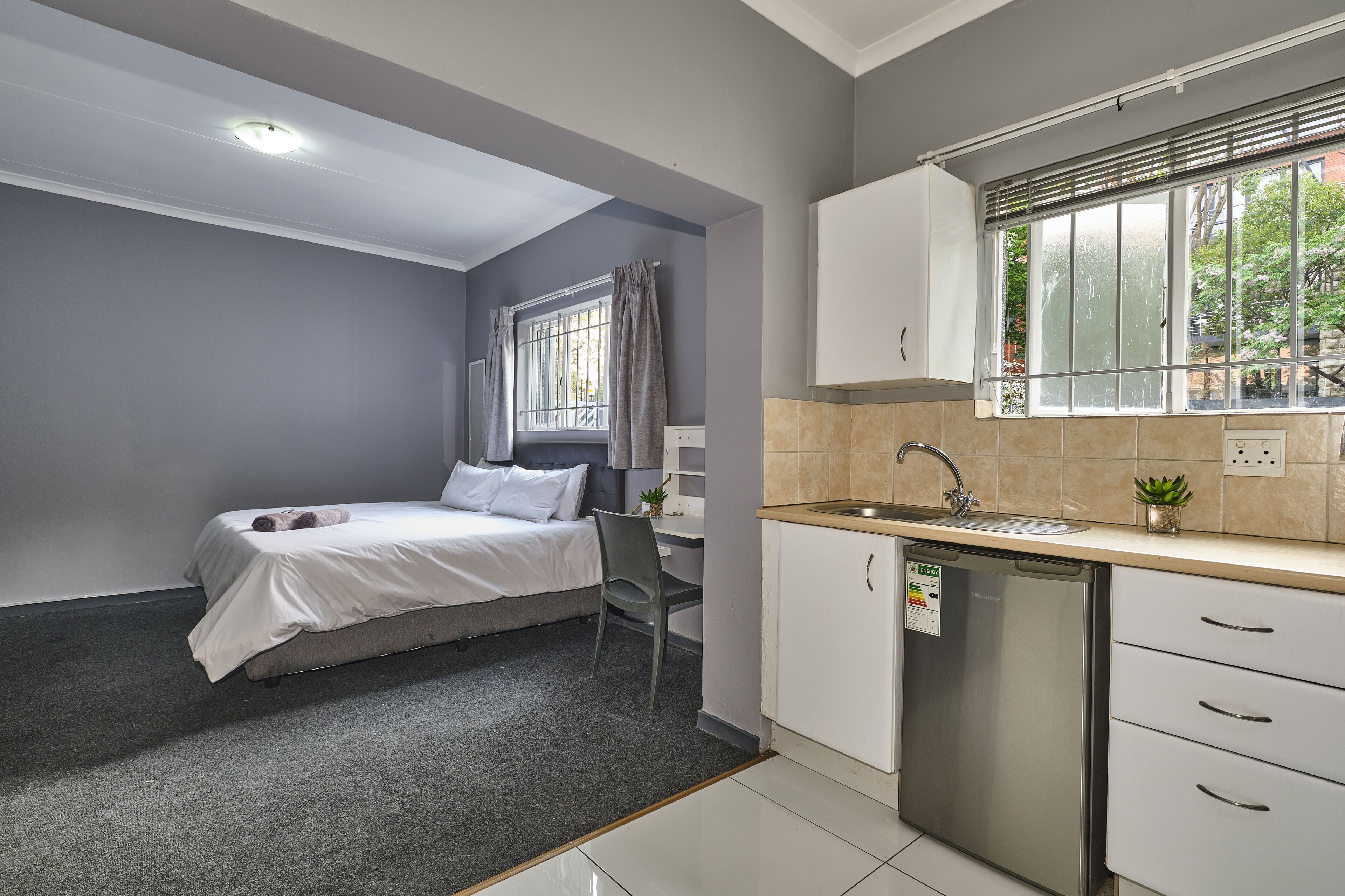 Una habitación pequeña con cama, escritorio, silla, lavamanos y lavavajillas.
