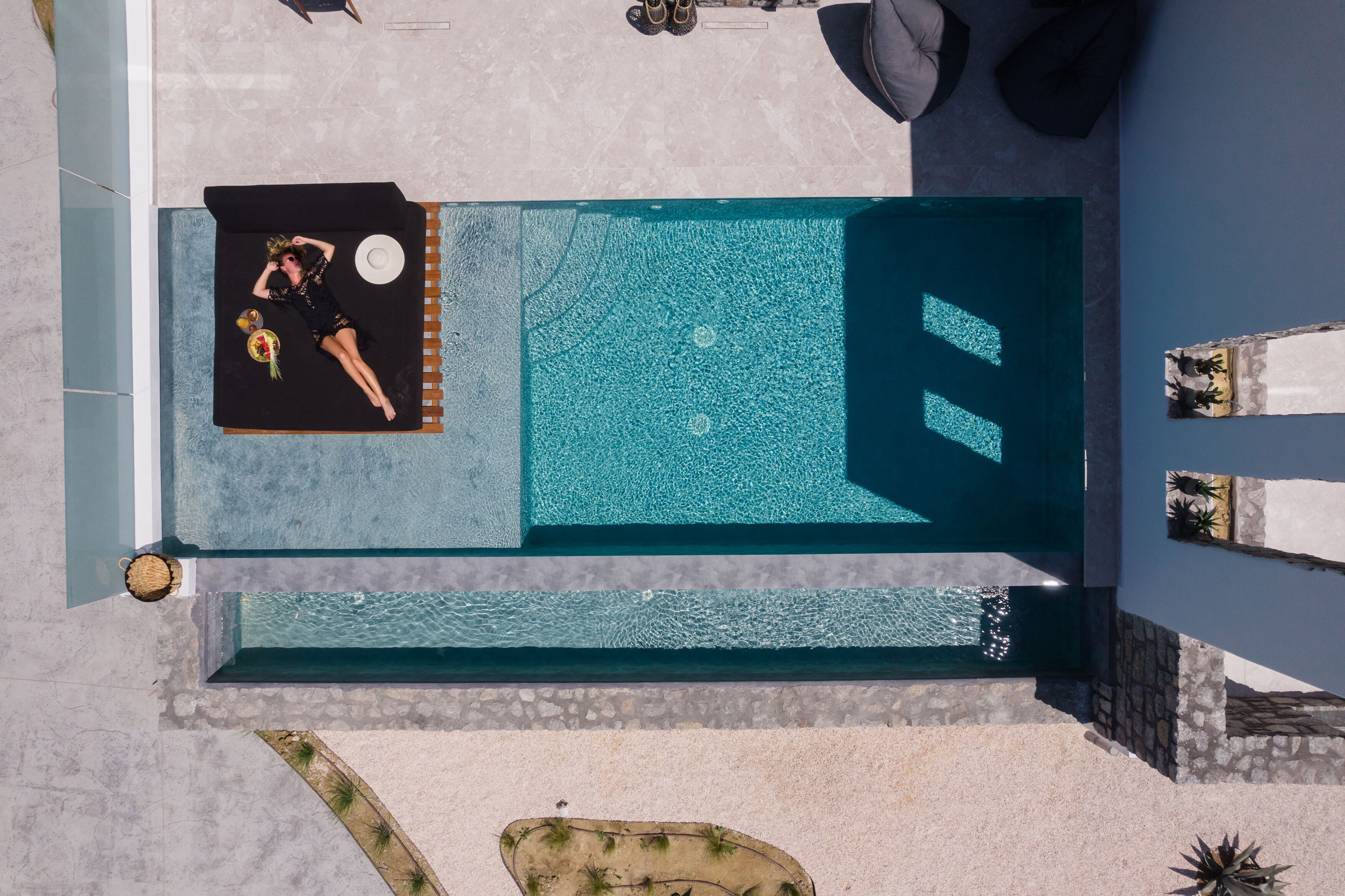 An aerial view of a swimming pool with a lounge area, a sunbed, and a small garden.