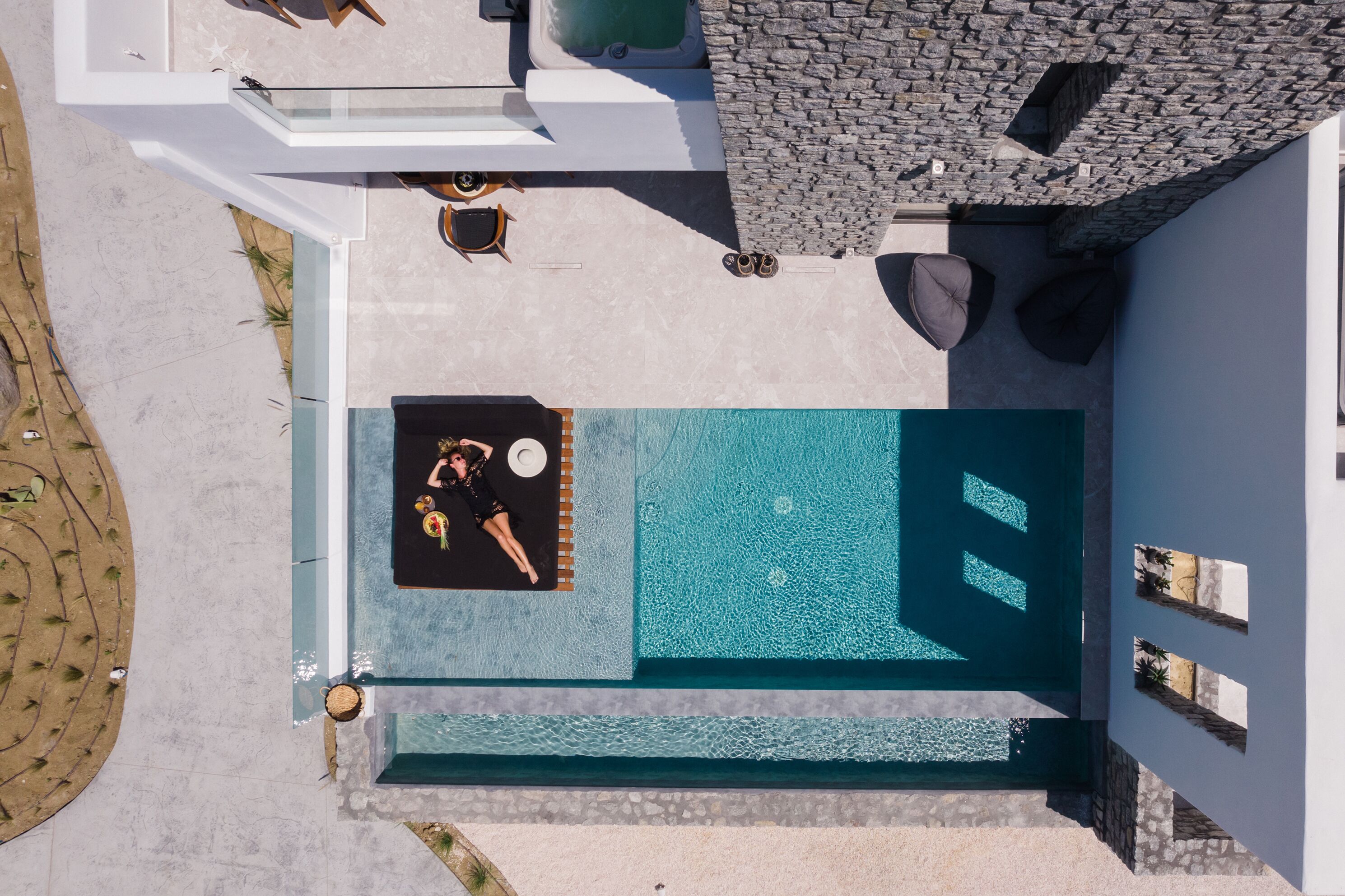 Vue aérienne d’un espace piscine extérieur moderne, comprenant un jacuzzi, des sièges et un mur en pierre.