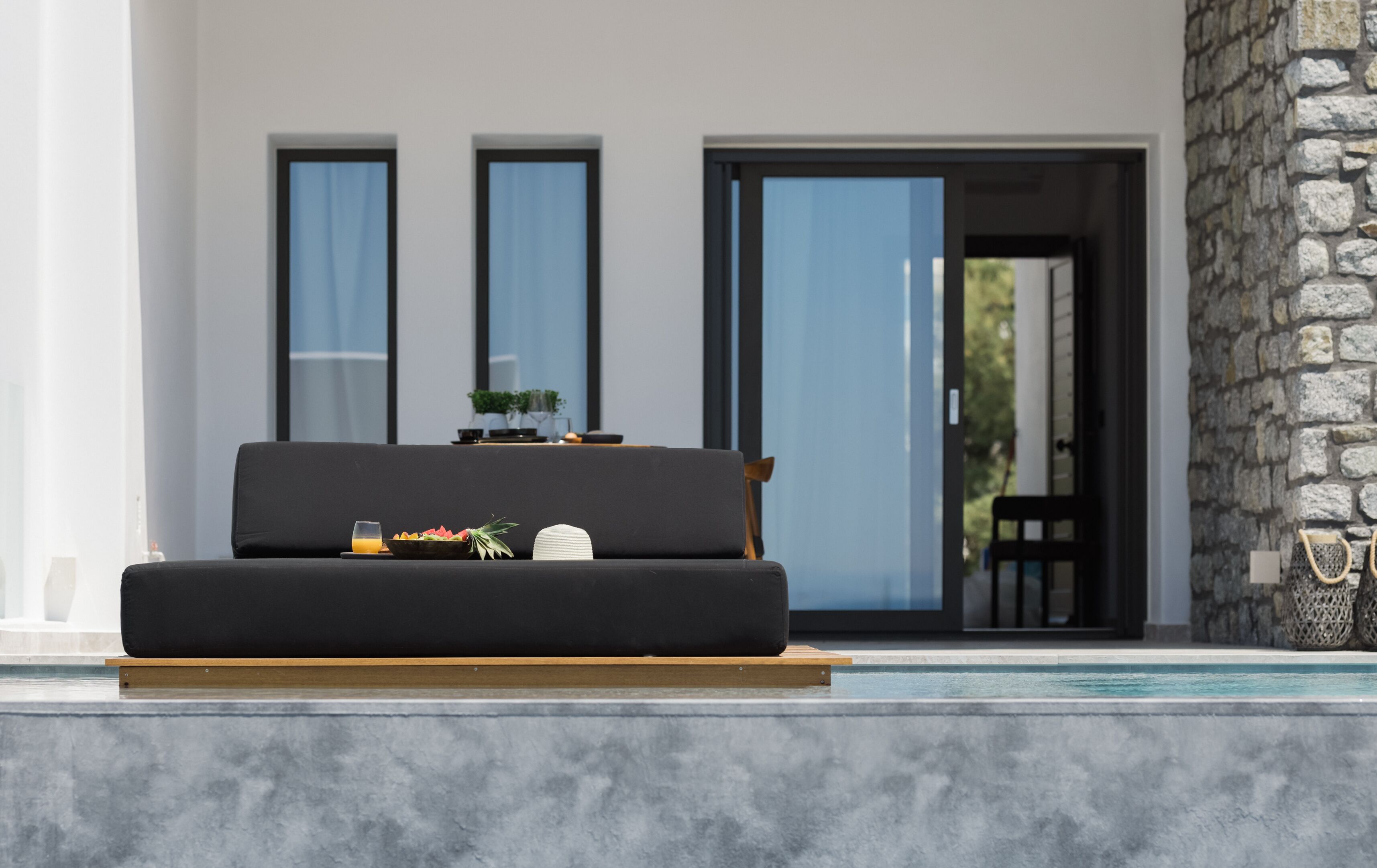 A modern outdoor seating area with a black sofa, a bowl of fruit, and a glass of orange juice.