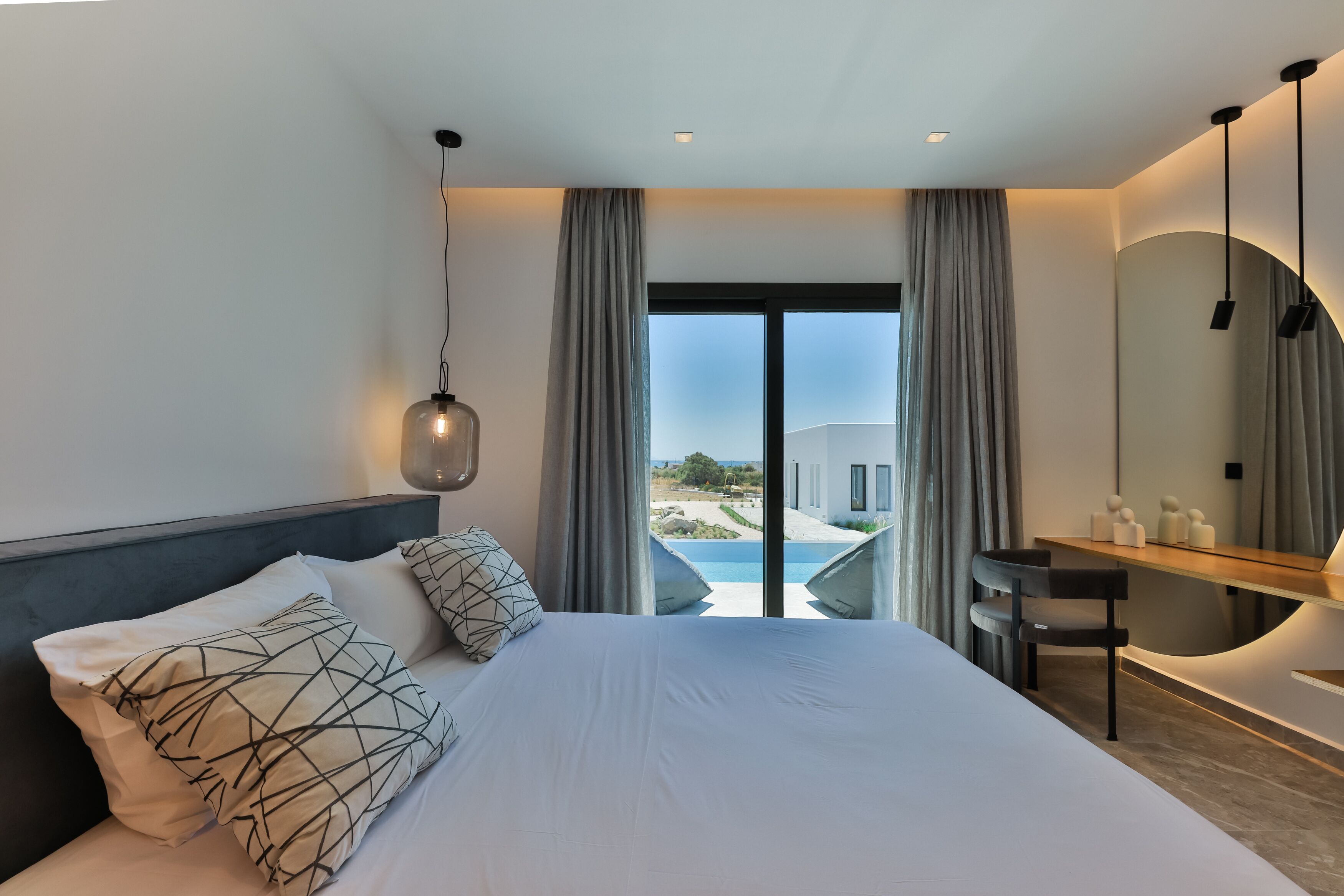 A modern hotel room with a large bed, a desk, and a view of a pool and building.
