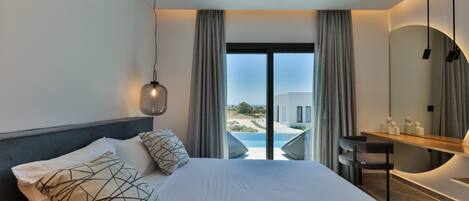 A modern hotel room with a large bed, a desk, and a view of a pool and building.