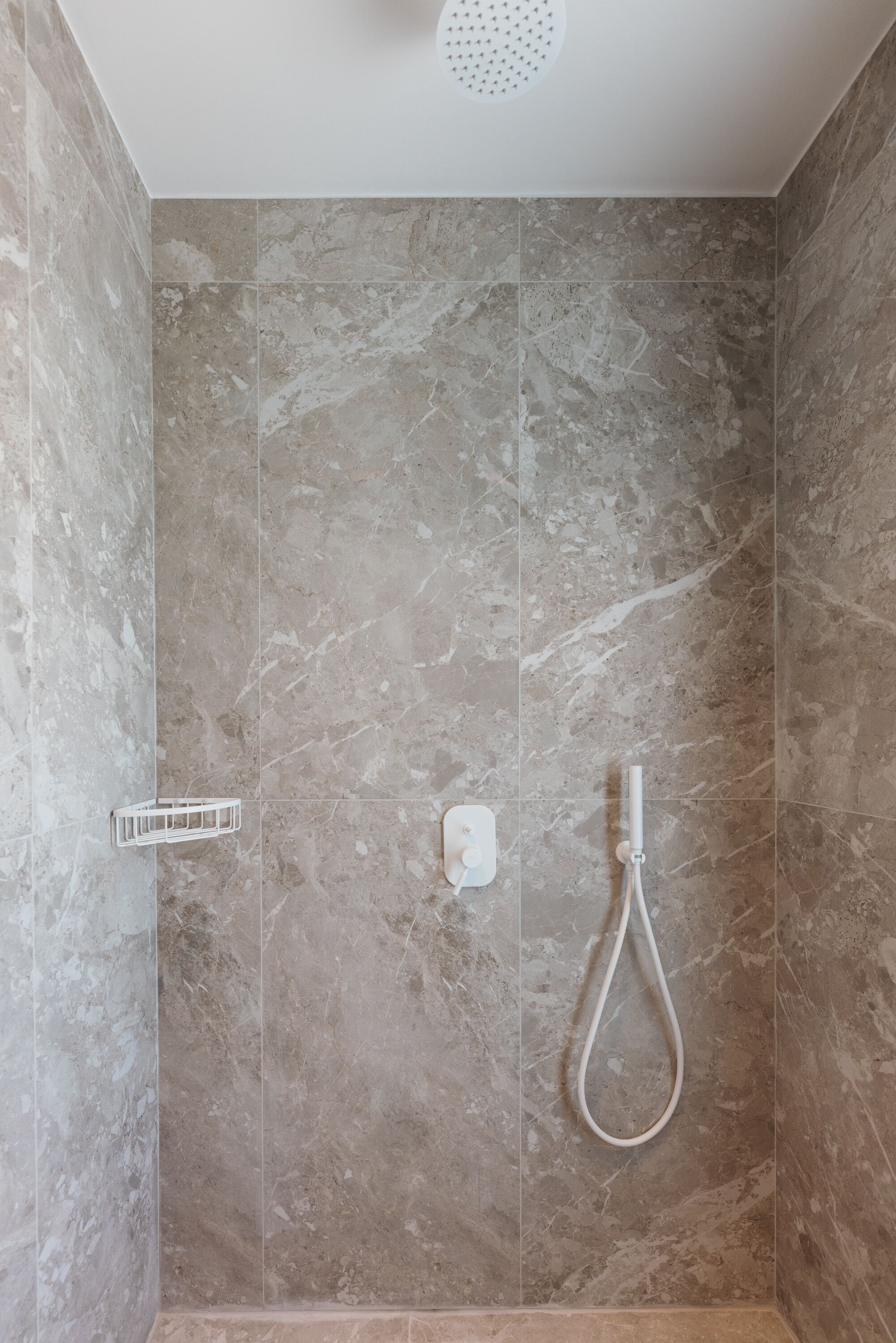 Eine Dusche mit Duschbrause, Seifenspender und einem weißen Handtuchhalter an einer gefliesten Wand.
