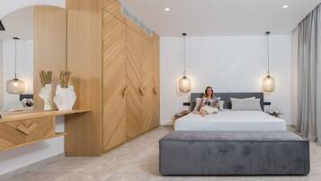 Un dormitorio moderno con una cama grande, un reposapiés gris, un armario de madera e iluminación colgante.