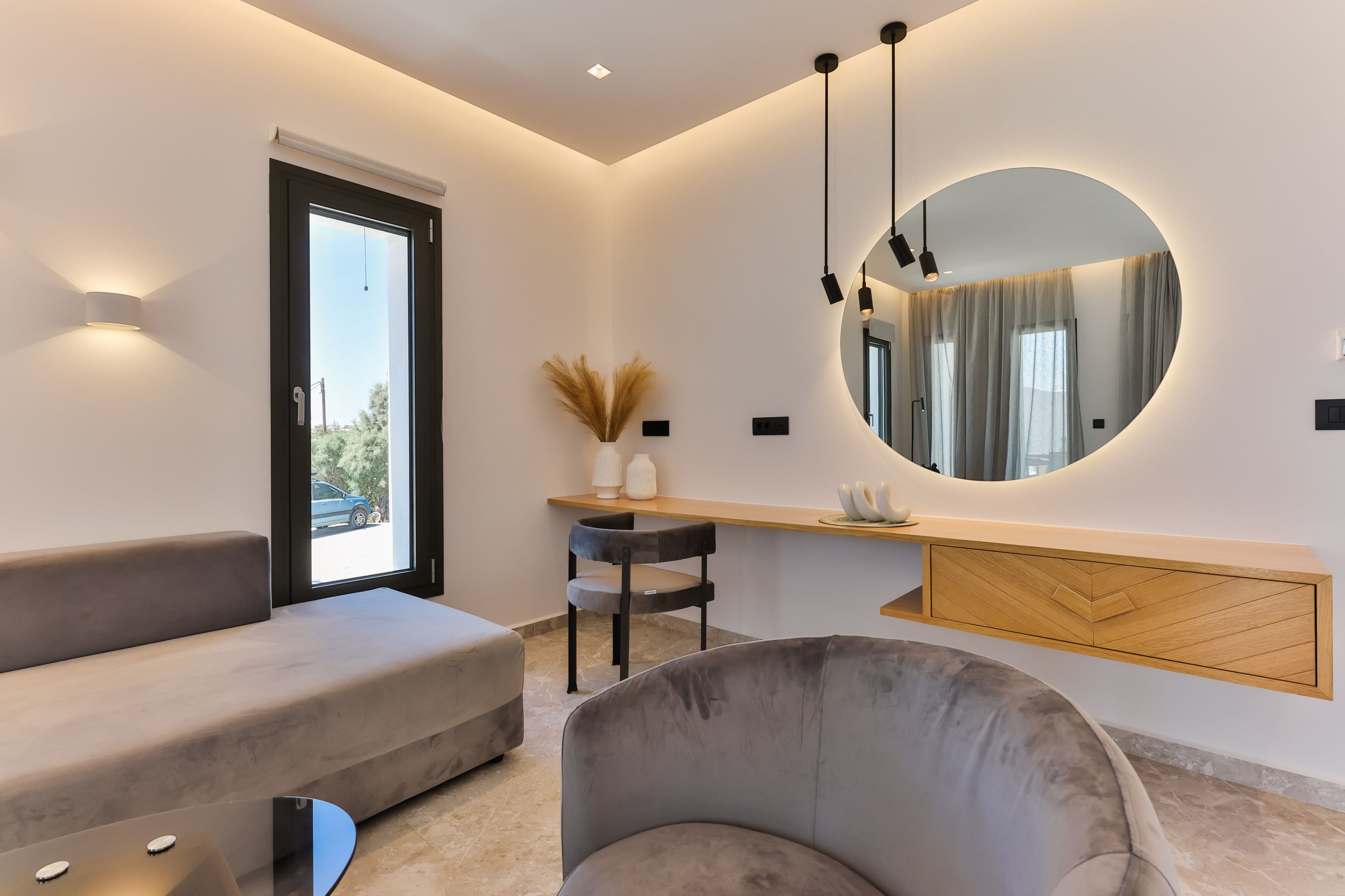 Una sala moderna con un sofá, una silla, un escritorio con espejo y un ventanal grande.