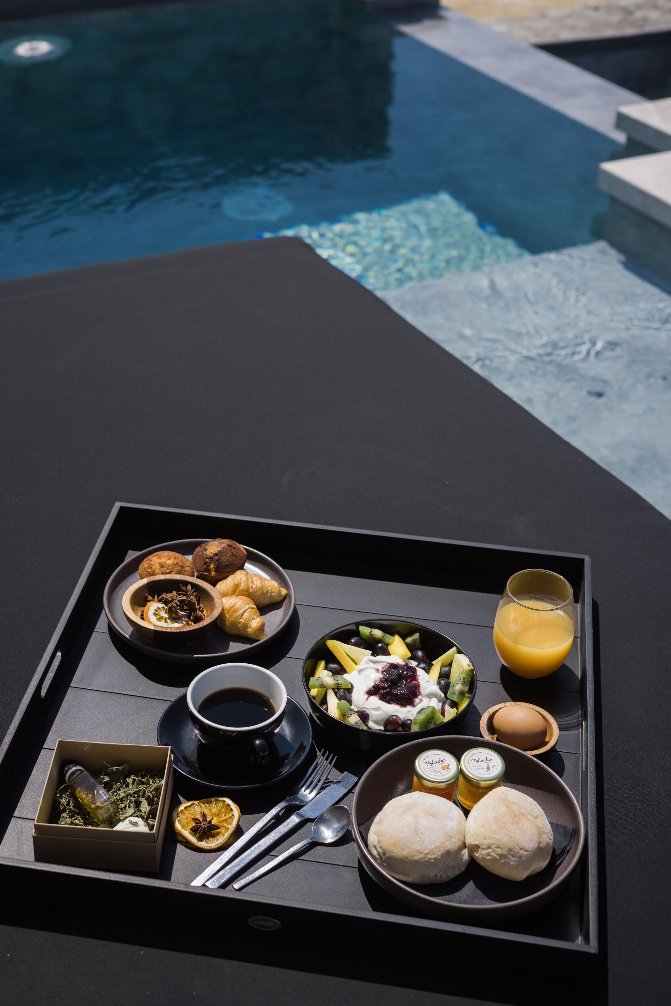 A tray with breakfast items including croissants, a bowl of fruit, a glass of orange juice, and a cup of coffee.