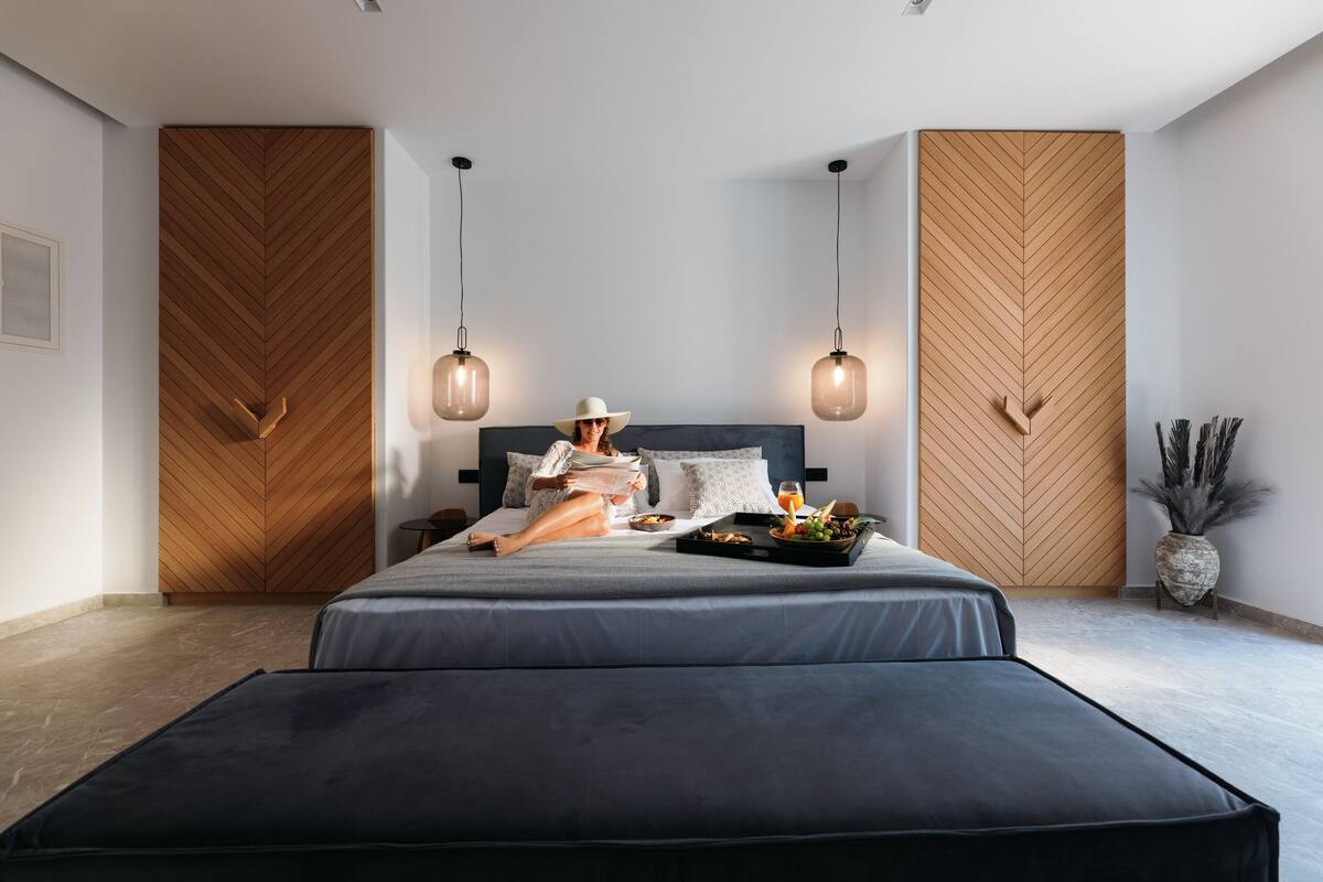 Ein modernes Schlafzimmer mit einem großen Bett, Holzwandverkleidung, Pendelleuchten und einem Nachttisch mit einer Vase.