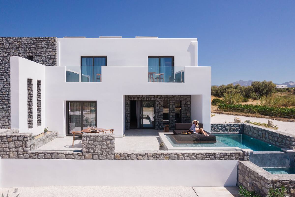Ein modernes, zweistöckiges Haus mit Natursteinfassade, Schwimmbad und Sitzgelegenheit im Freien.