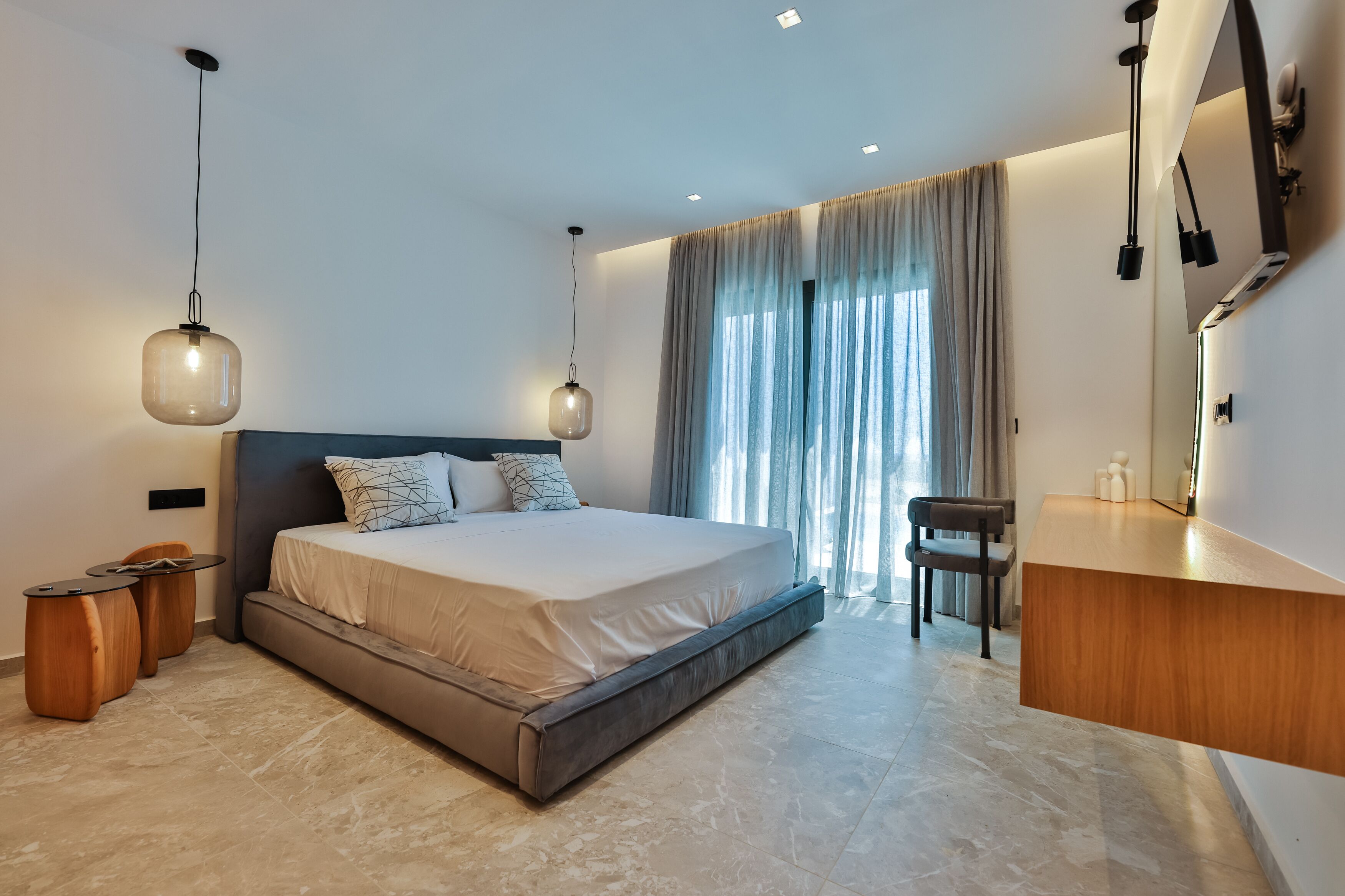 A modern bedroom with a large bed, bedside tables, a chair, and a built-in wooden console table.