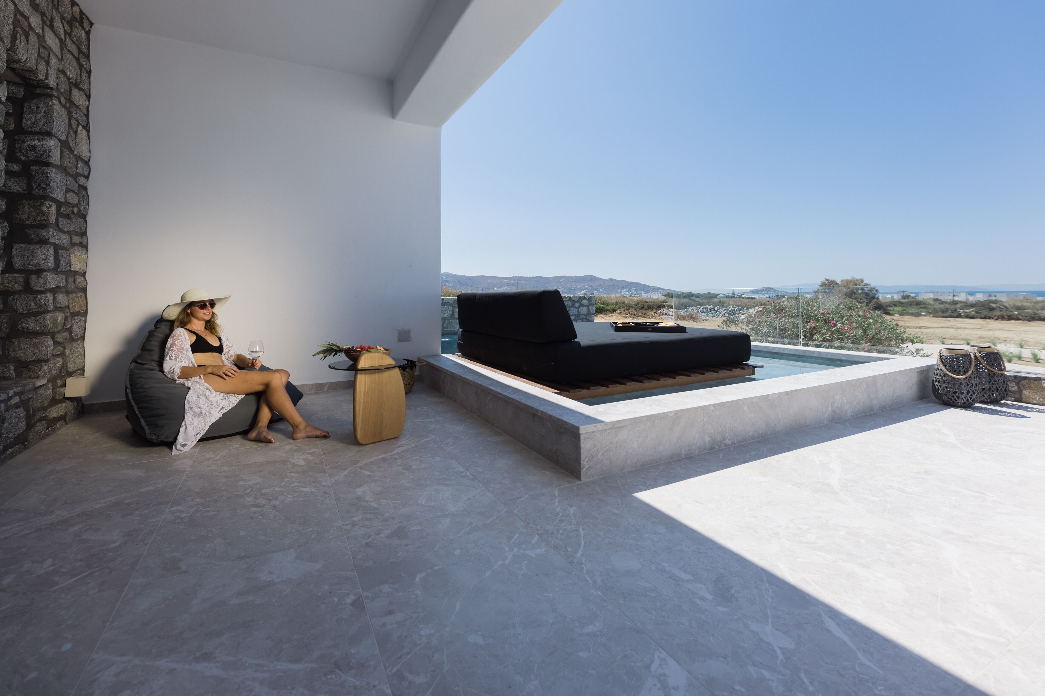 A modern outdoor seating area with a stone wall, a black sofa, and a view of the landscape.