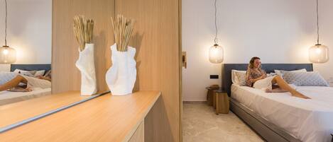 Ein modernes Hotelzimmer mit einem Holzbüro, zwei Nachttischen, einem großen Bett mit grauem Kopfteil und zwei Pendelleuchten.