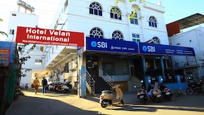 Hotel Velan International, an SBI bank branch, and parked scooters in front. - Hotel Velan International  (Krishnagiri)