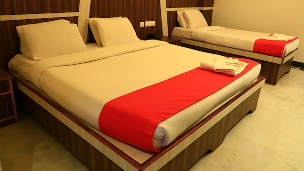 A double bed with a red blanket and a single bed with a red pillow. - Hotel Velan International  (Krishnagiri)