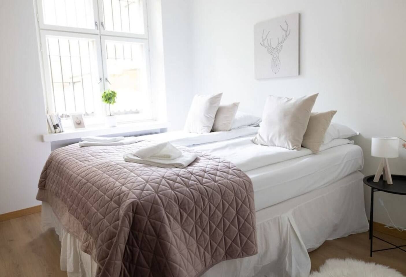 Une chambre à coucher avec un lit, des oreillers, une table de chevet, une lampe, une fenêtre et une œuvre d’art murale.